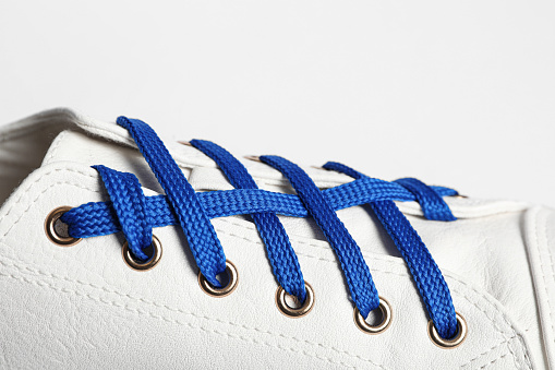 Stylish shoe with blue laces on white background, closeup