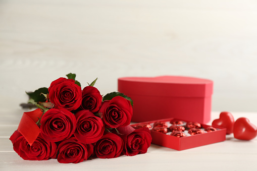 Beautiful red roses, sweet candies, decorative hearts and gift box on white table. St. Valentine's day celebration