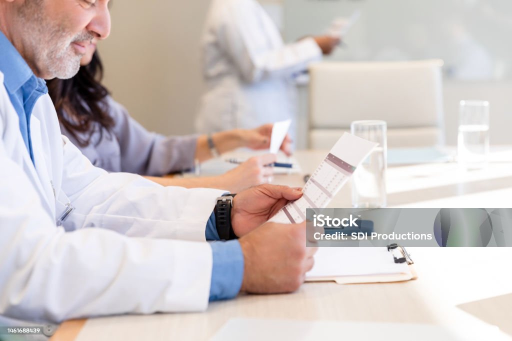 Bored mature doctor reviews spreadsheet during presentation The focus of the photo is on a bored mature adult doctor as he reviews the spreadsheet for the meeting. Boredom Stock Photo