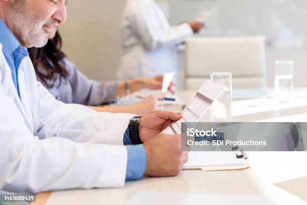 Bored Mature Doctor Reviews Spreadsheet During Presentation Stock Photo - Download Image Now