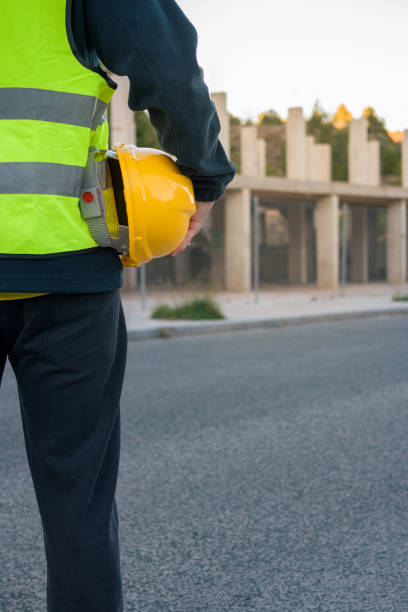 istock Unrecognizable worker with yellow hard hat in hand observes a building under construction 1461688441