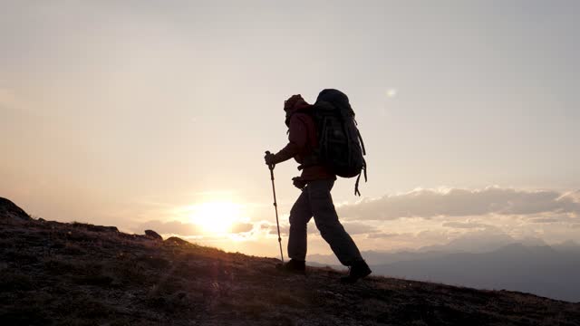 Hiker Climber Climbs Up To Top Cliff Of Mountain With Backpack At Sunset
