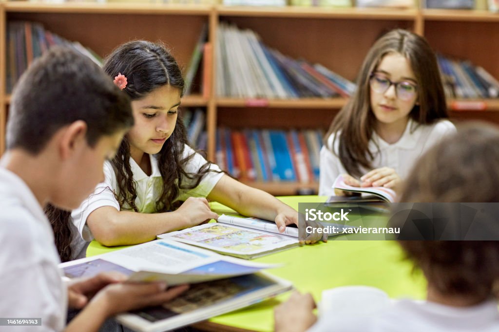 Elementary students reading in library Waist-up view of 9, 10, and 11-year old schoolboys and girls in uniforms sitting together and exploring literature and graphic novels. Boys Stock Photo