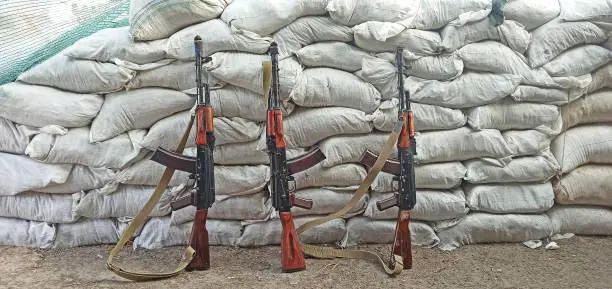 Photo of Three Kalashnikovs standing near sandbagged fortifications. AK-74 outdoor