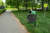 A garbage can in a park near the sidewalk.