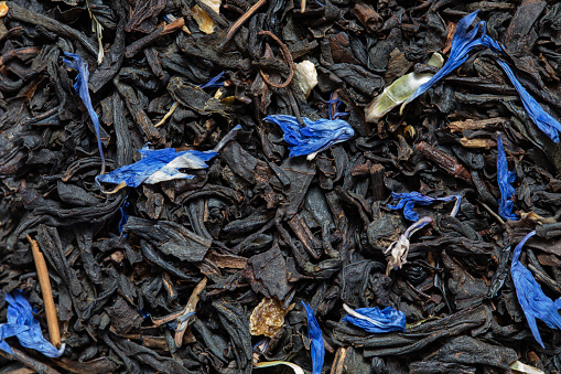 Closeup of black tea with orange, lemon peels and cornflower petals background for design purpose