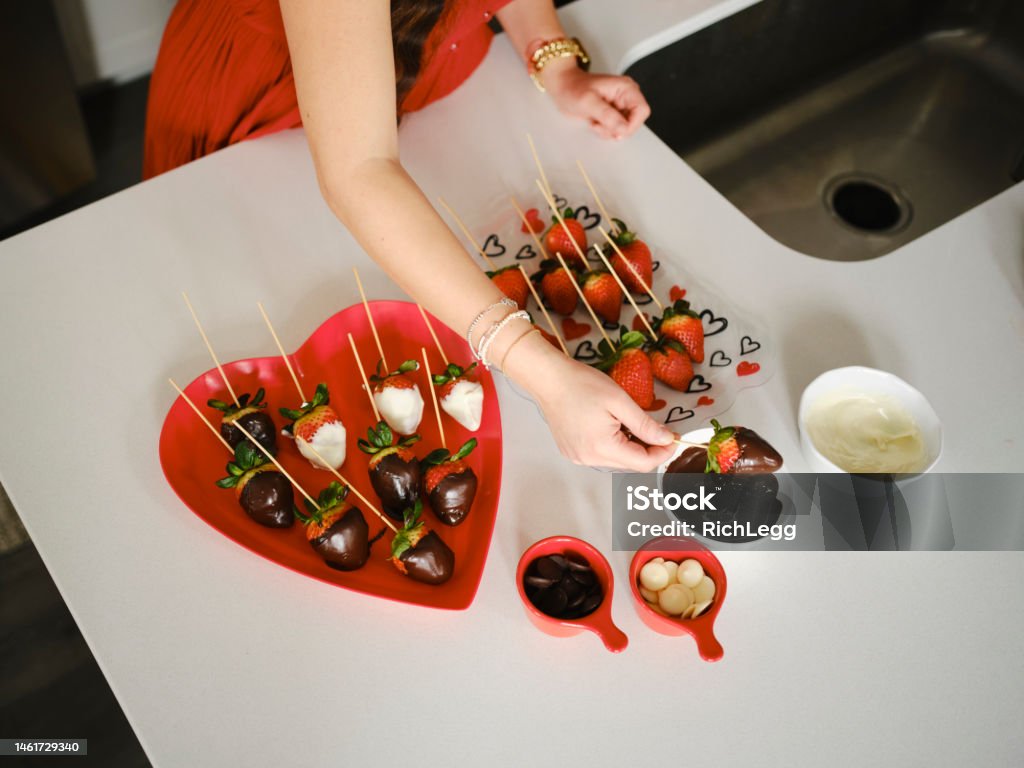 Family Valentines Day Celebration Making Chocolate Strawberries A hispanic family making chocolate dipped strawberries in a home kitchen. Chocolate Dipped Stock Photo