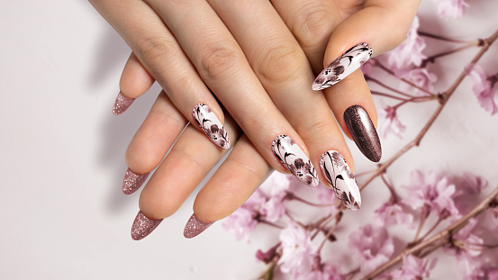 Flower nail design. Brown manicure on sharp long nails close-up on a flower background with painted flower design.