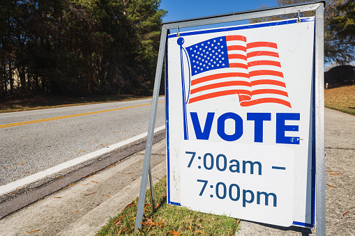 A sign by road gives the hours available to vote at that voting precinct.