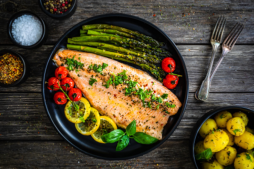 Fried salmon fillet, asparagus and fried tomatoes on wooden background