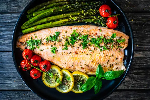 Photo of Fried salmon fillet, asparagus and fried tomatoes on wooden background