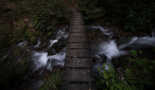 Long exposure of simple wooden footbridge path walkway over white water river stream in Nelson Lakes National Park Tasman South Island New Zealand