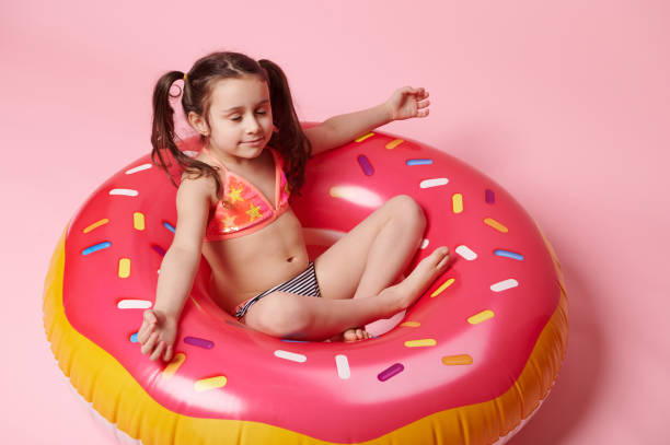 menina criança adorável meditando na posição de lótus em um donut de anel de natação inflável cor-de-rosa, sobre o fundo da cor rosa - swimming tube inflatable circle - fotografias e filmes do acervo