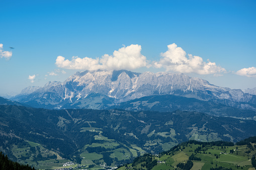 Panorama of the high rocky mountains of the Dachstein massif in Austria with a deep valley with green meadows.