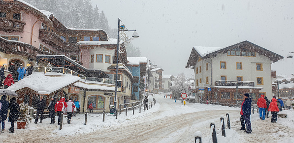 Italy, Canazei - 23 January, 2023: Incidental people in ski garments walking on street while heavy snowing. Small touristic town Canazei in Dolomites.