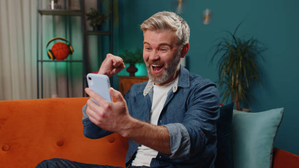 istock Middle-aged old man at home use smartphone typing browsing wow yes found out great big win celebrate 1461789391
