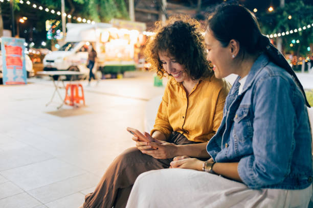 istock Two Happy Beautiful Women Watching Something On Mobile Phone While Sitting Outdoors At Night 1461794126