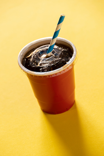 This is a studio shot of a red plastic soda cup with a drinking straw on a yellow background