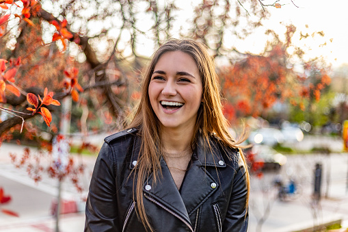 Madrid, Spain. Cool and funny young smiling woman in urban setting surrounded by red leafy trees at sunset