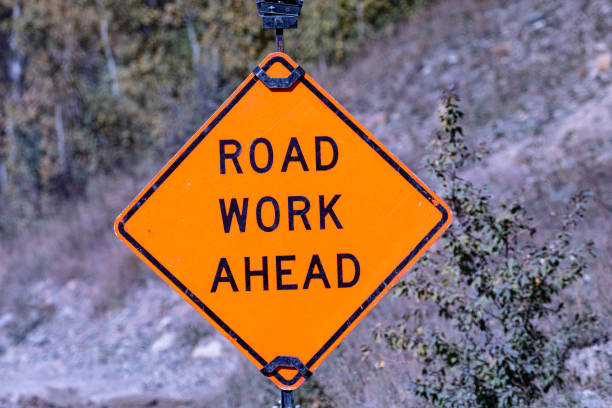 Battered, but clearly legible, road safety sign warns ROAD WORK AHEAD in Glacier National Park, Montana, United States