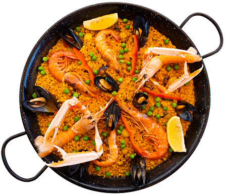 Portion of fresh seafood paella served on plate with piece of lemon. Isolated over white background
