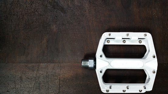 on a dark wooden background - a white bicycle pedal Flat Pedal with steel spikes with empty space