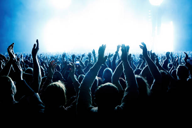 una multitud de personas con los brazos levantados durante un concierto de música con un increíble espectáculo de luces. siluetas negras - concierto fotografías e imágenes de stock