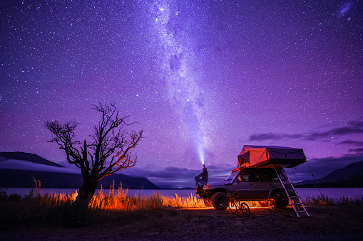 Beautiful and dramatic landscape scenery of a camper van with a man sitting on it enjoying starry night by the Lake Ohau, Mackenzie Basin, South Island, New Zealand.