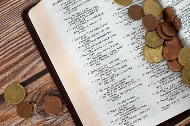 Coin money on open Holy Bible. Concept of Christian tithing, religious offering, and contribution to church of God Jesus Christ. Old Testament proverbs book.