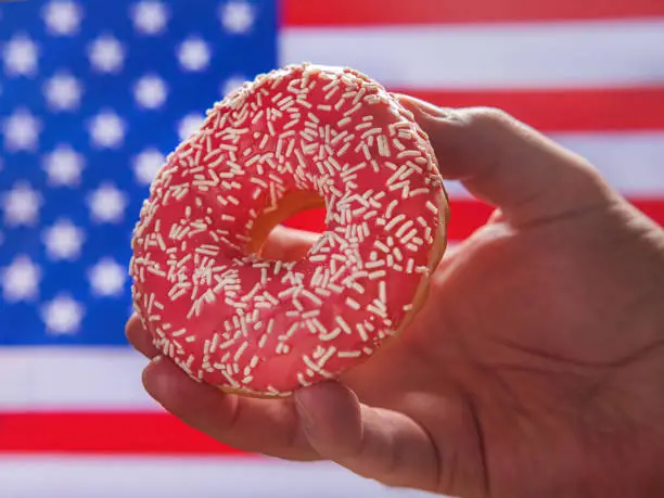 Pink delicious donut in the male hand against US Flag