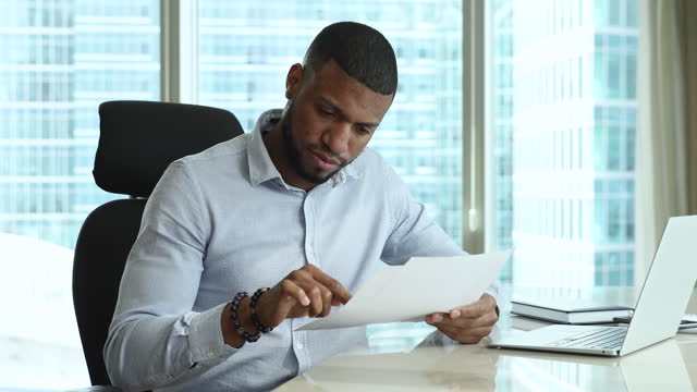 Serious focused African employee man holding document, receiving letter