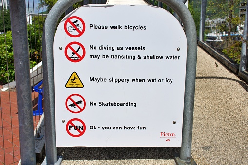 Picton, New Zealand - January 17th 2023. Not Allowed Sign on bridge to Picton Marina. The sign states: Please walk bicycles, no diving as vessels may be transiting & shallow water,  may be slippery when wet or icy, no skateboarding, no fun - OK you may have fun.