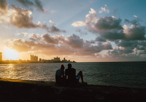 Havana, Cuba - December 9th 2022: The Malecón, Old Havana, Cuba, with local Cuban residents and visitors relaxing and walking afternoon promenades. Featuring a broad esplanade, roadway, and seawall, the Avenida de Maceo is a famous place and tourist destination. People travel to view the Caribbean Sea waterfront, national capital city urban skyline, and community culture.