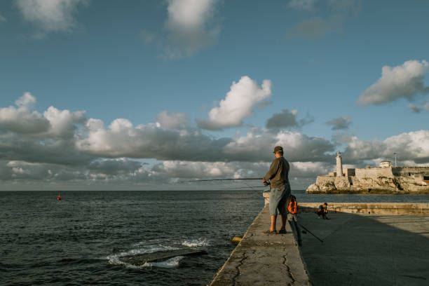 Havana, Cuba - December 10th 2022: The Malecón, Old Havana, Cuba, Fisherman at the entrance of the Havana bay, in front of the Morro Castle. Malecon is one the most popular attractions in Havana both to tourists and locals.