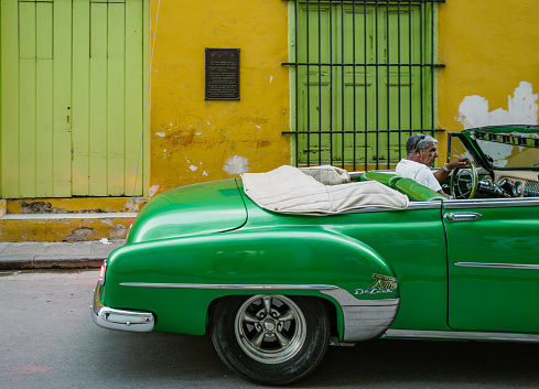 Havana, Cuba - December 10th 2022: Classic vintage cars driving along at old Havana. Old Havana is one the most unique and charming places for tourists in the world for its time-capsuled buildings and lifestyles.