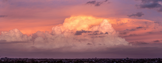A large moody cloud formation is brightly lit by the sun with the suburbs of Melbourne, Australia below