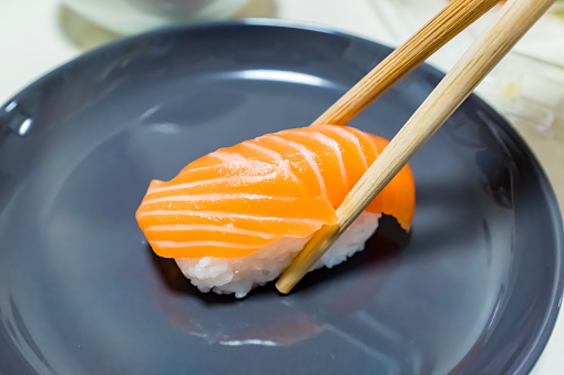 Wooden chopsticks hold salmon sushi