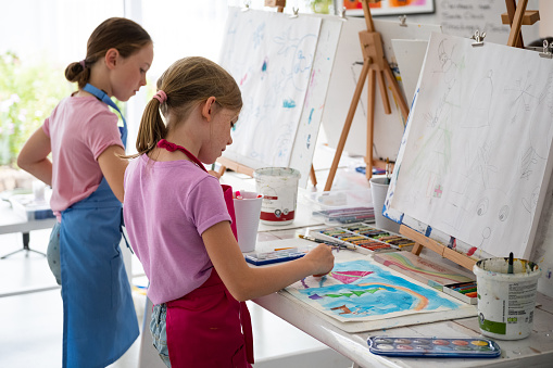 Two young girls enjoy drawing and painting during their fun art class. Fun art class with my friends