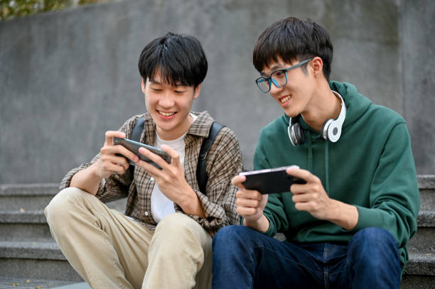 Happy young Asian man college student playing mobile game on his smartphone with his friend stock photo