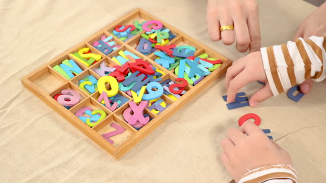 Closeup of hand mother and son playing alphabet games with plastic toys into the word with anxiously for improve mental health and memory, learning concept, weekend activity .