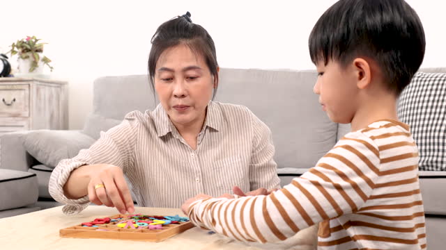 Asian happy single mother and handsome son playing alphabet games with plastic toys into the word with anxiously for improve mental health and memory. family spending time together in holiday.