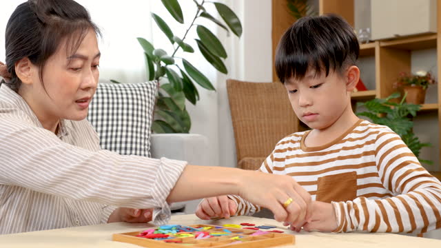 Asian happy single mother and son playing alphabet games with plastic toys, mom helping child learn foreign language for improve mental health and memory. family spending time together in holiday.