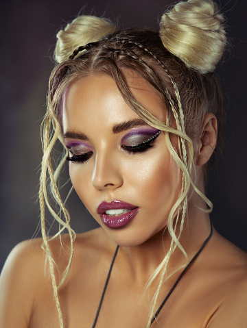 Beauty Girl with Stylish Eye Makeup and Purple Lipstick. Model Face Closeup with Glitter Eyeshadow on Closed Eyes. Sexy Woman with Two Space Buns Hairstyle over Dark studio Background