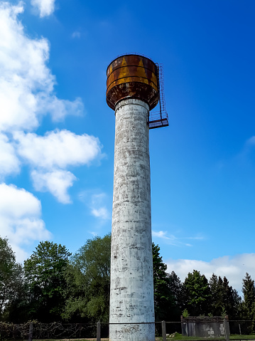Old water tower construction in concrete and rusty metal with nature and bright blue sky background. Photo taken in Latvia