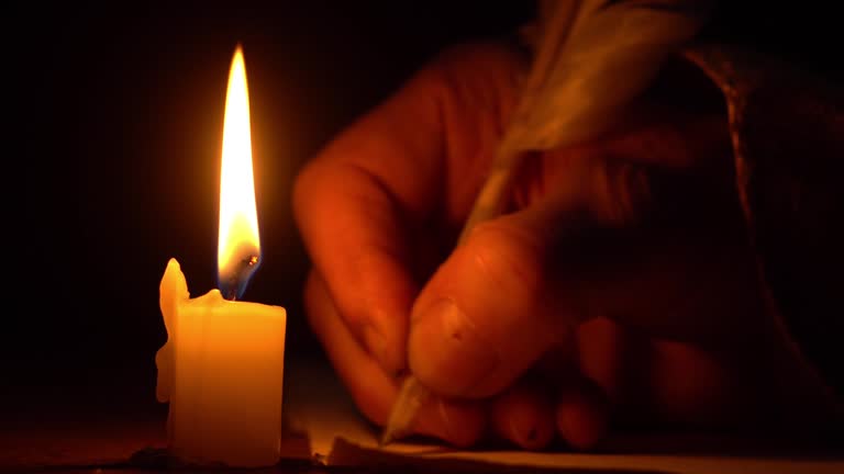 A hand writing in a quill pen by a candle