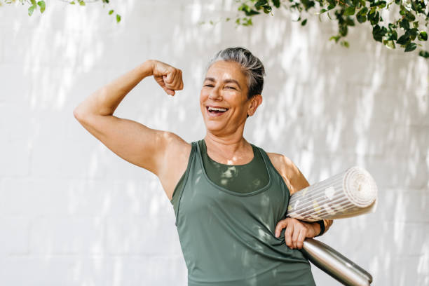 in forma e orgogliosa: la donna senior sfoggia il suo bicipite mentre celebra i suoi risultati di fitness - sports clothing practicing success vitality foto e immagini stock