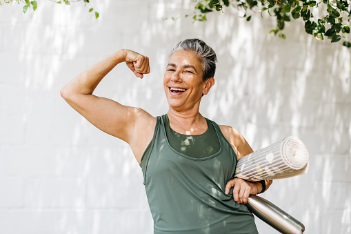 Senior woman flaunting her strong bicep and looking at the camera, celebrating her fitness achievement after a workout session. Happy elderly woman taking pride in her fitness journey and the physical strength she has achieved.