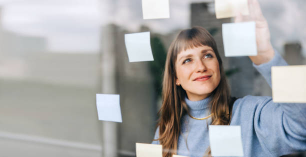 istock Young female entrepreneur sticking adhesive notes to a glass wall 1462023034