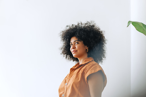 Young businesswoman looking away thoughtfully while standing in an office. Businesswoman with Afro hair working in a modern workplace.