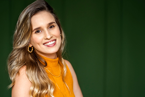 Portrait of a confident young female architect standing in front of a green wall in office and smiling